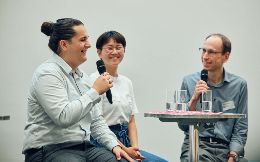 Nikola Knežević on a panel at the opening of the Lifelong Learning Center at the University of Bern, holding a microphone and speaking alongside a fellow student and a professor.
